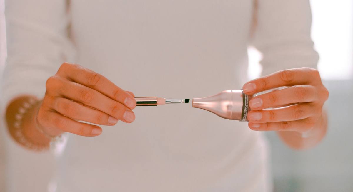 Close-up of a nail pattern grinder shaping an acrylic nail with fine dust particles, demonstrating controlled motion near the cuticle