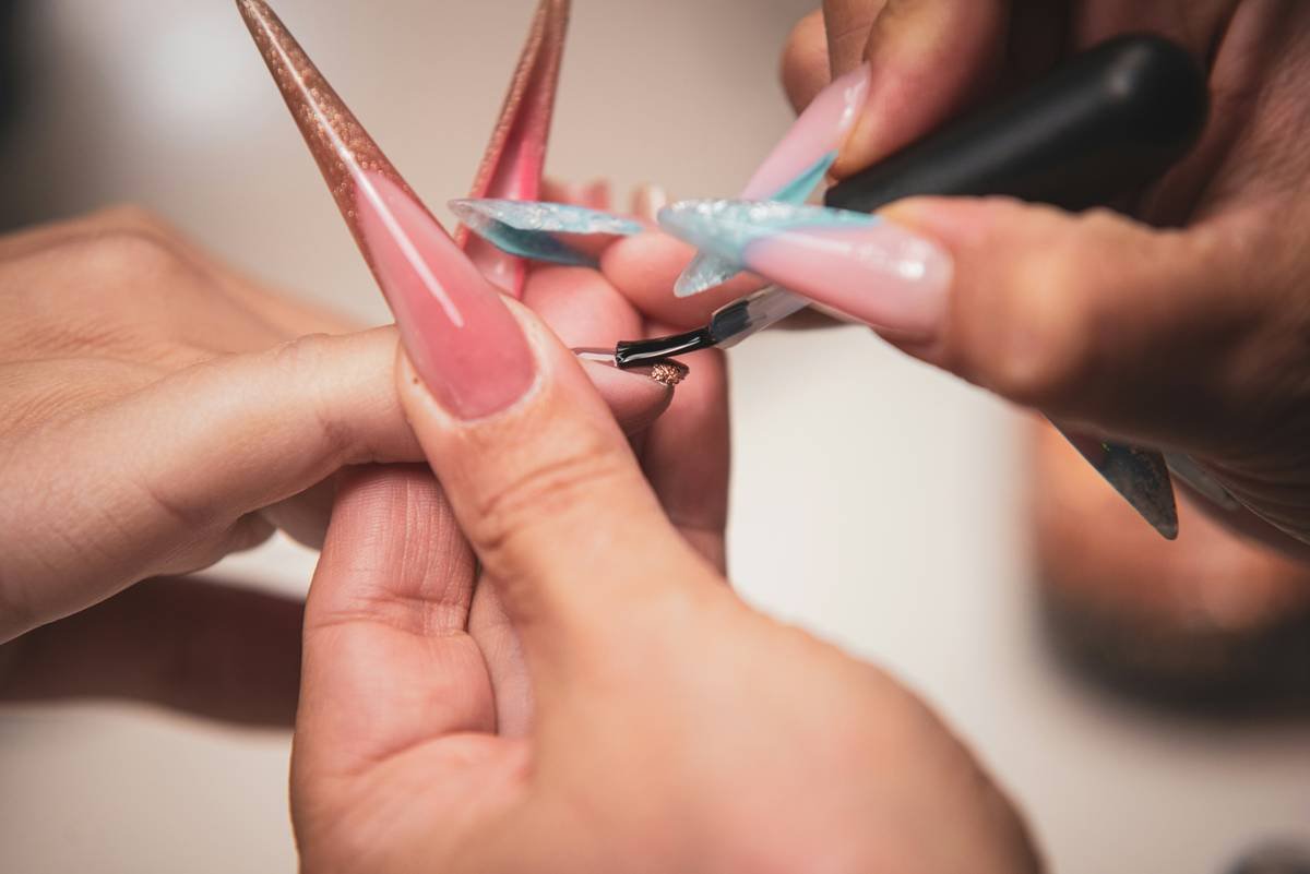 Professional technician using a salon nail grinder on a client's hand with proper lighting and ergonomic posture
